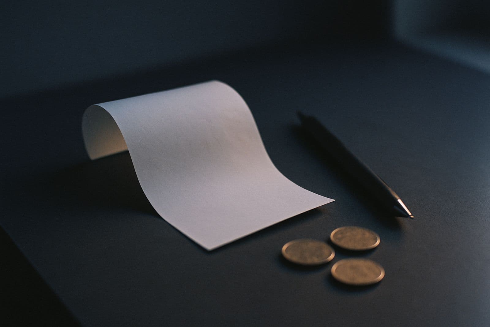 A blank receipt, a pen and a few coins on a dark desk