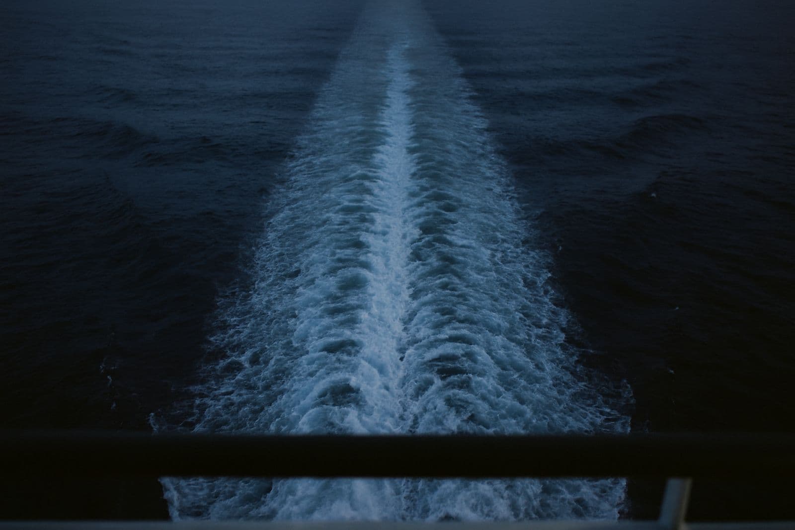 A long white wake on dark open ocean at dusk