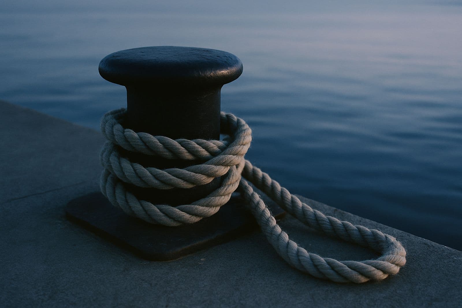 A mooring rope looped around a bollard on the pier at dawn