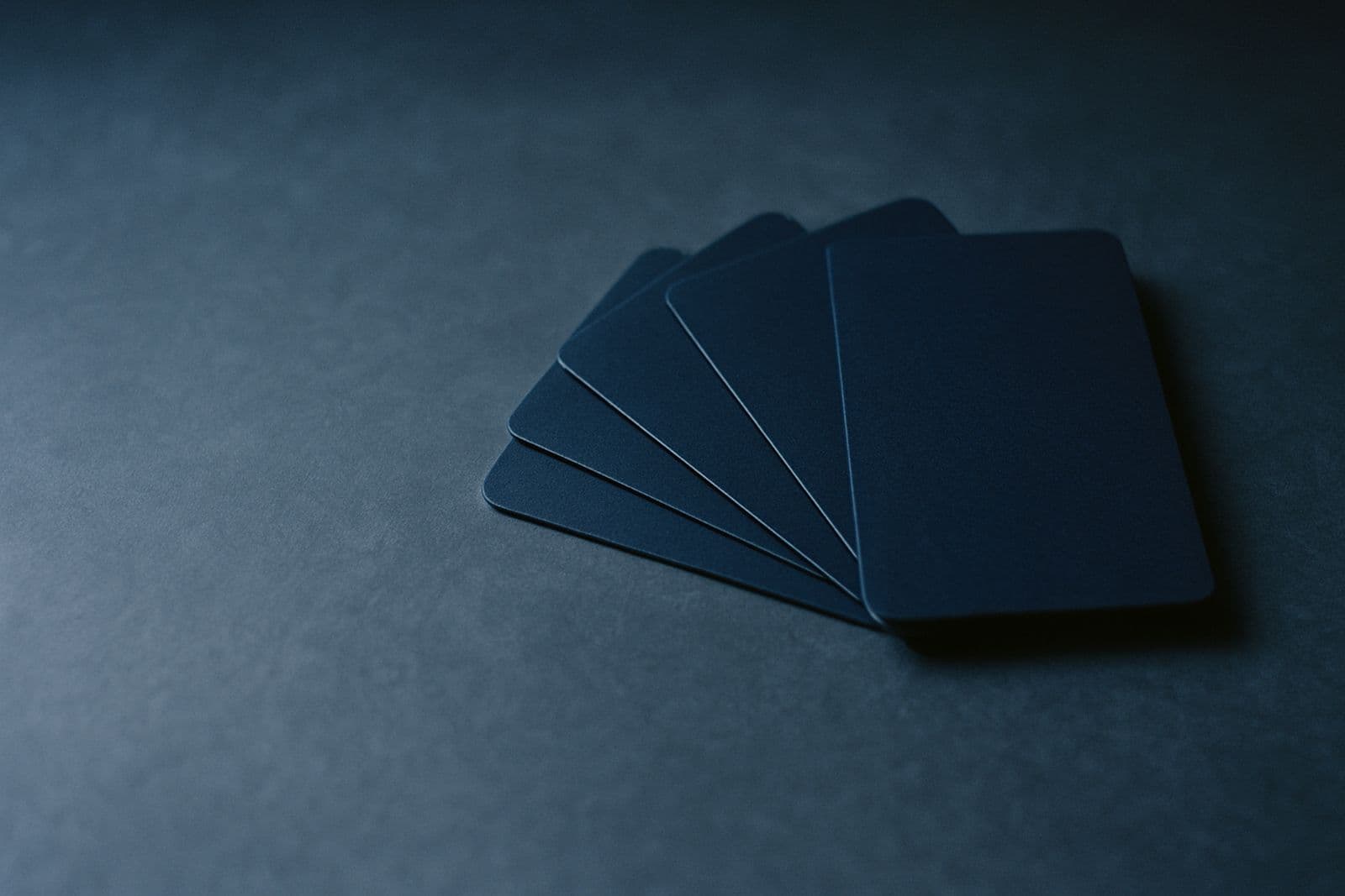 A fanned stack of plain dark-blue cards on a slate desk