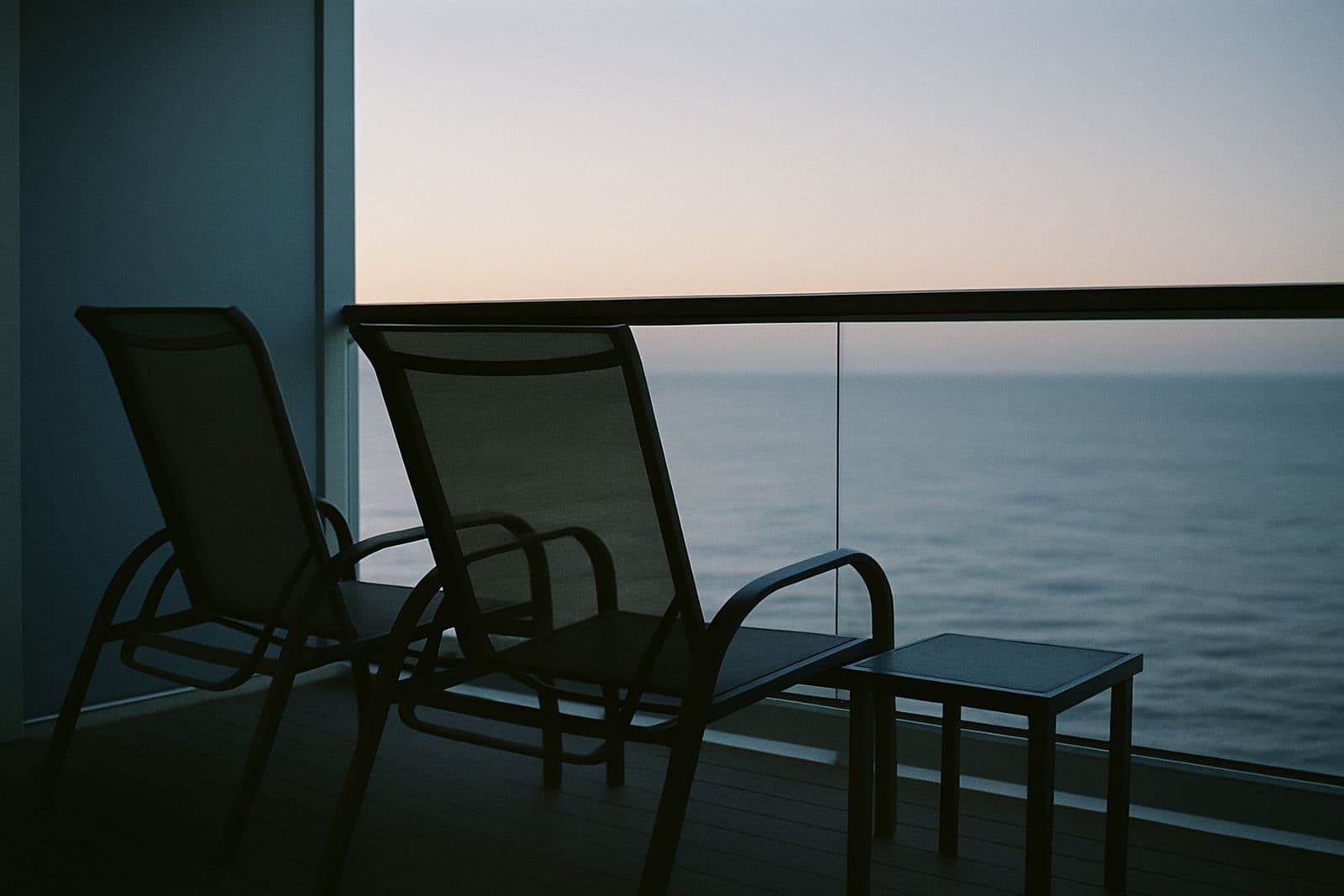 Two lounge chairs on a private balcony facing a calm sea